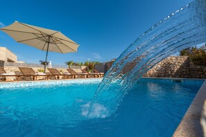 Ein Pool mit Wasserspiel, Liegestühlen und einer Steinmauer.