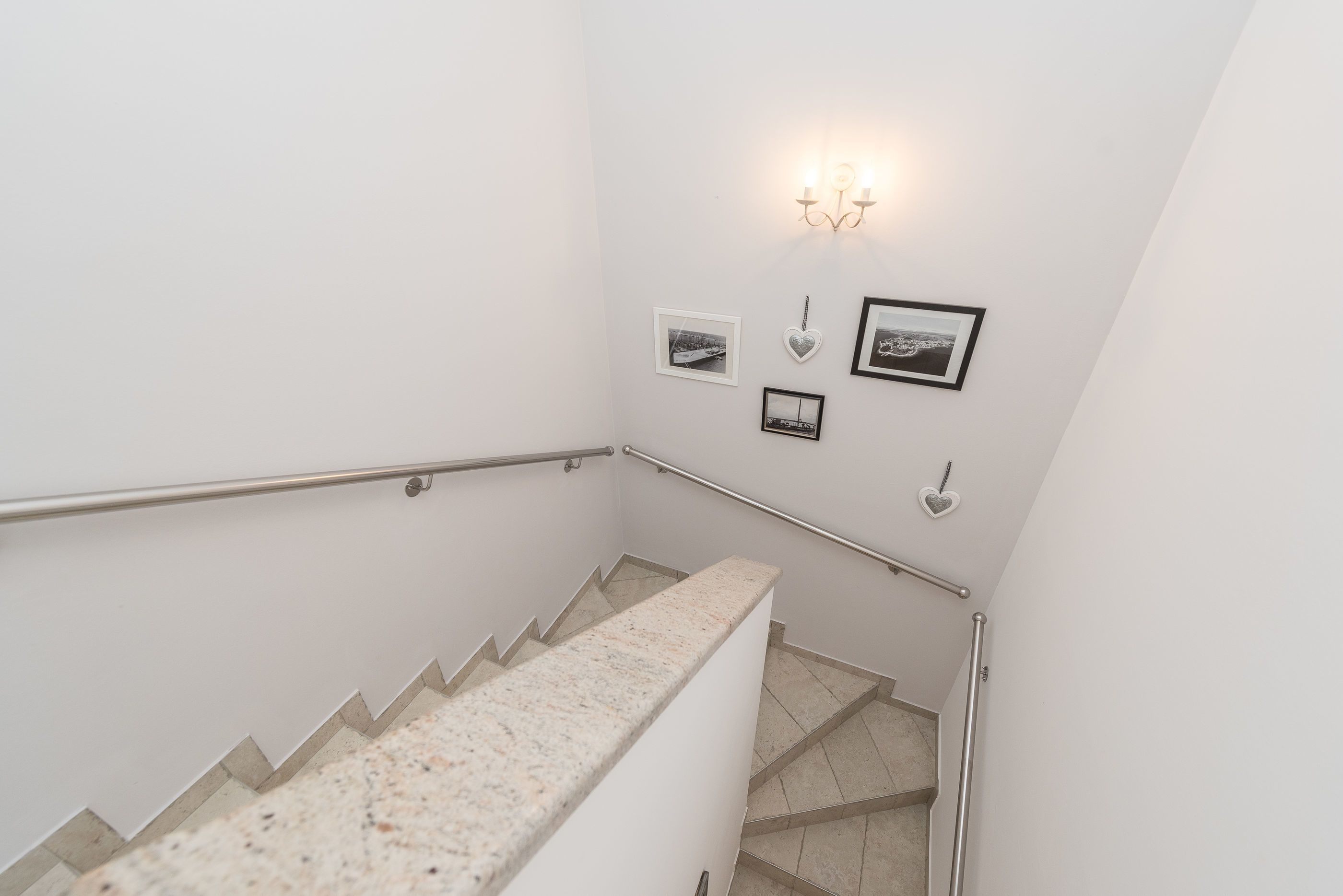 A staircase with a handrail, a wall-mounted light fixture, and several framed pictures.