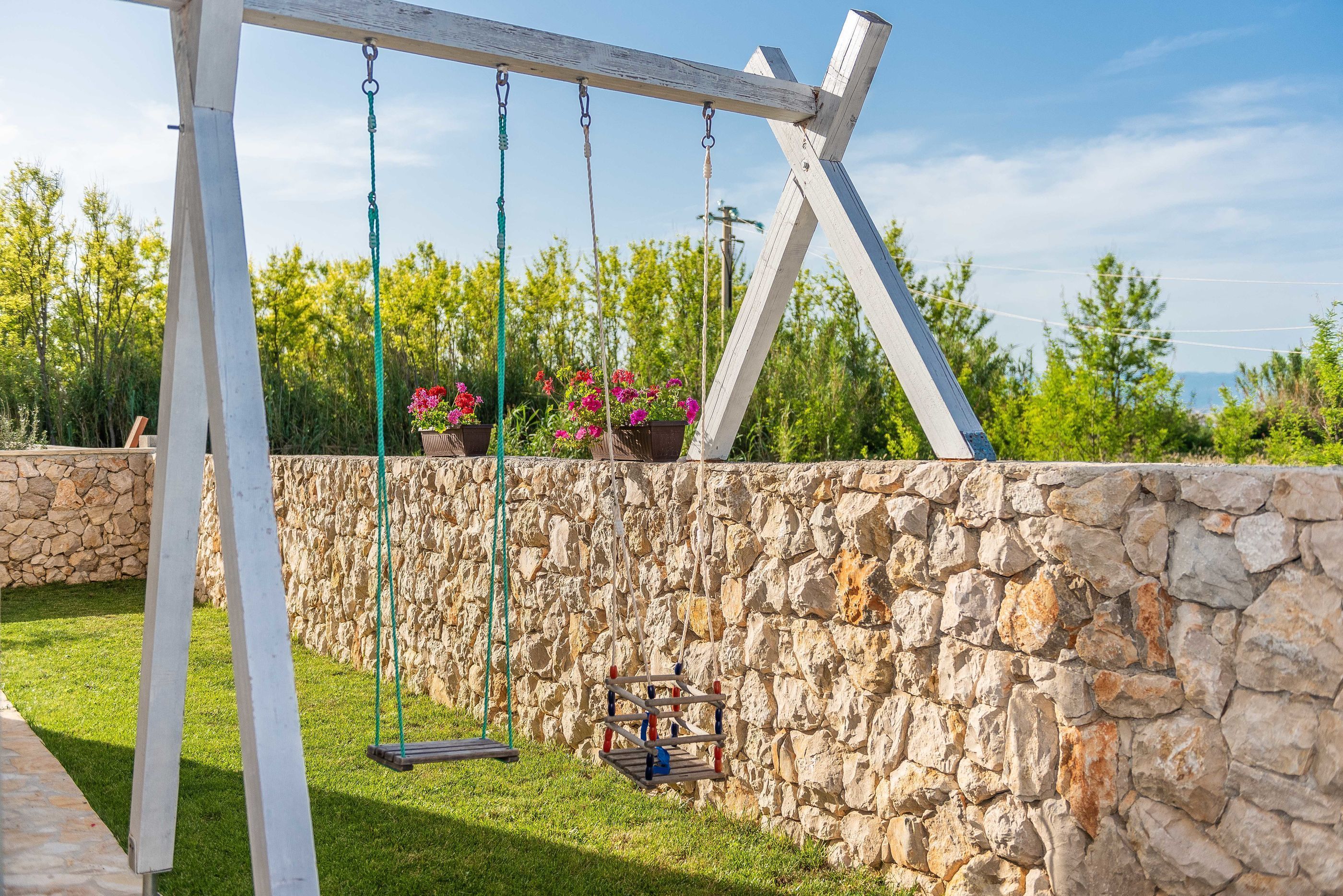 A wooden swing set with a stone wall and greenery in the background.