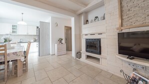 A modern kitchen with white cabinets, a dining area with a table and chairs, a fireplace, and a TV mounted on the wall. - Villa Kirstin (Privlaka)