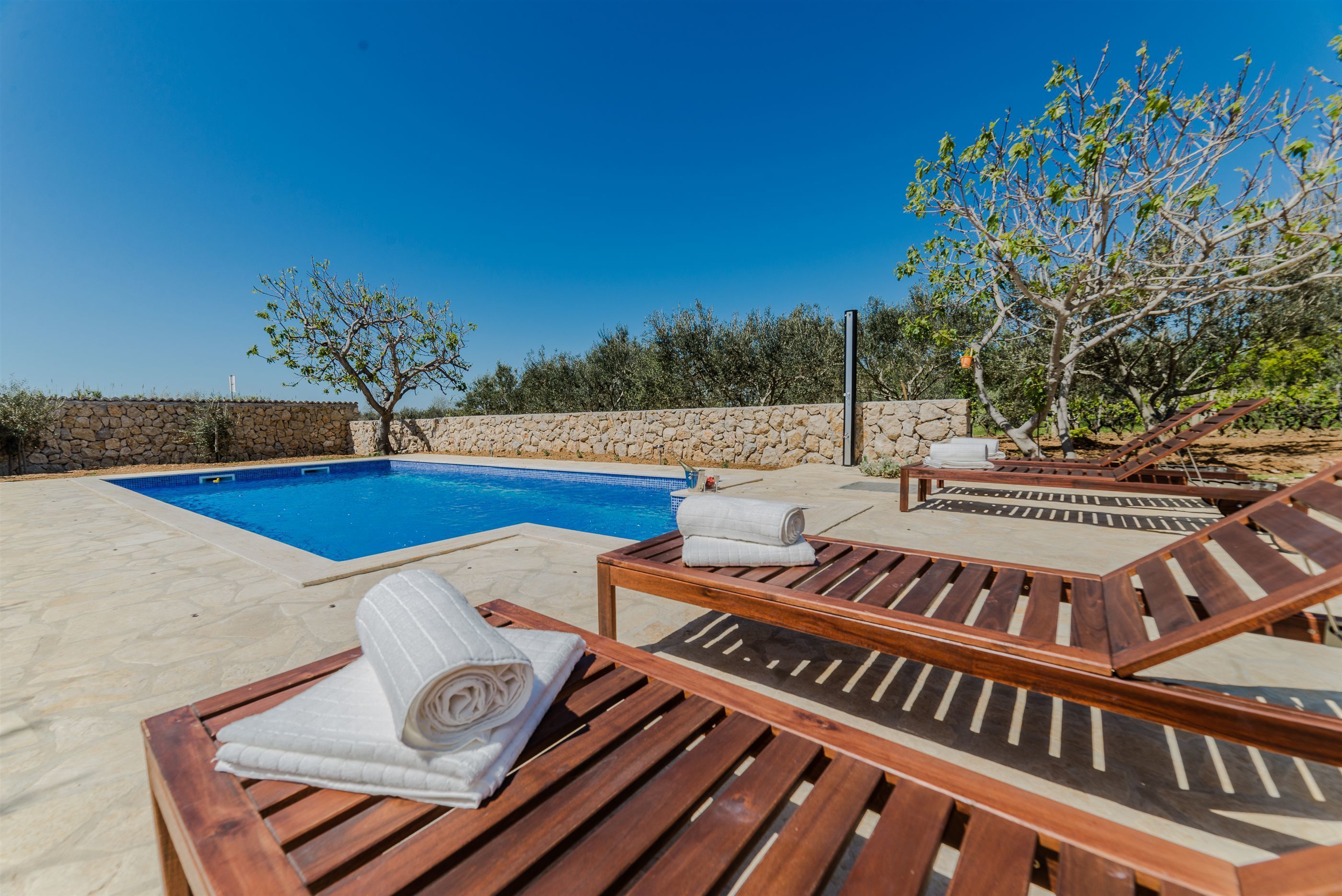 A poolside area with wooden lounge chairs and a stone wall.