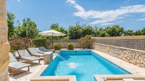 A rectangular swimming pool with a stone border, surrounded by lounge chairs and a white umbrella. - Villa Karin (Privlaka)