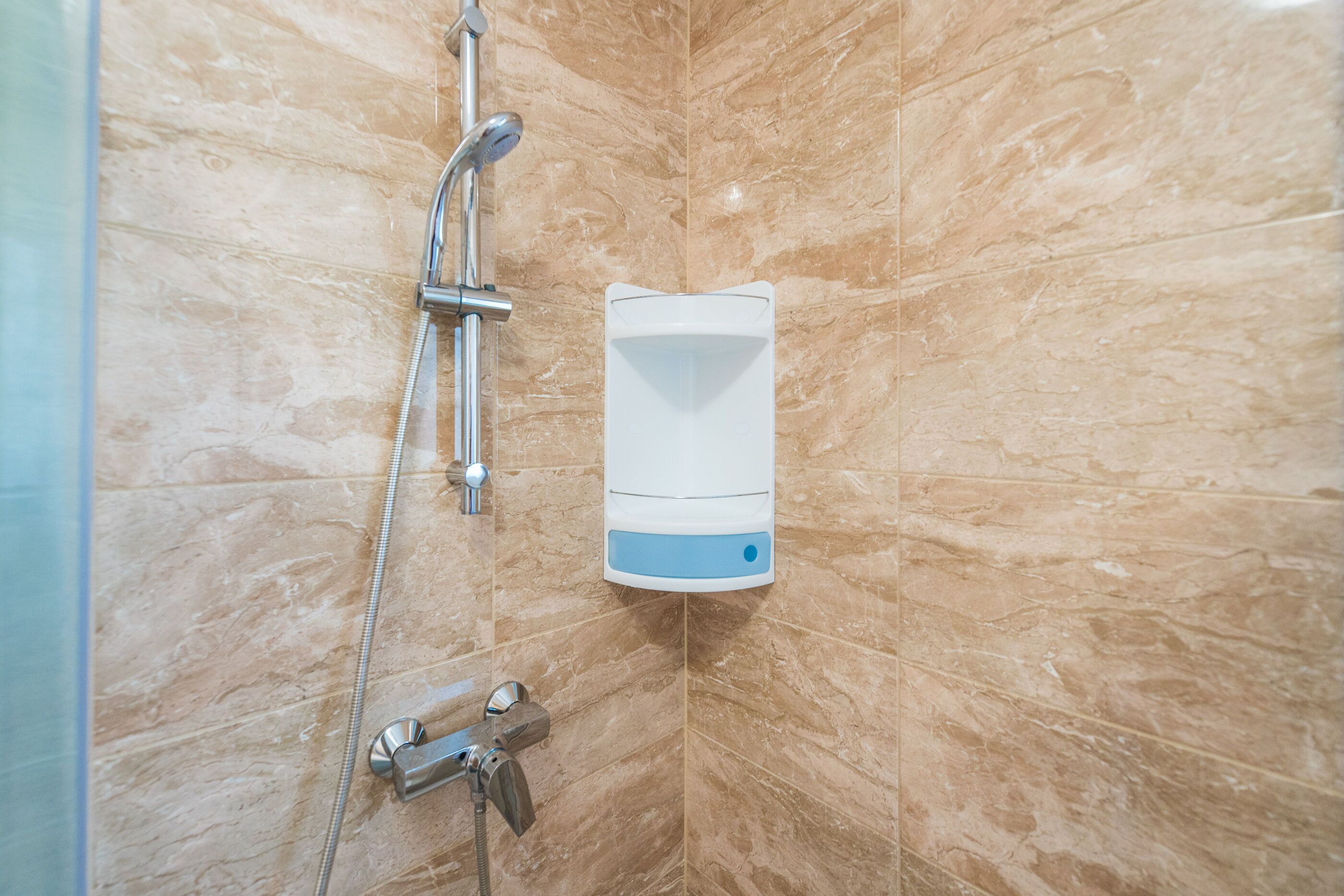 Un baño con ducha, cabezal de ducha de mano y dispensador de jabón en la pared.