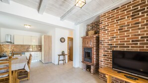 A modern living room with a brick fireplace, a TV on a wooden stand, and a dining area with wooden furniture. - Villa Karin (Privlaka)