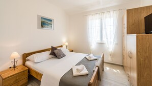A bedroom with a bed, nightstand, lamp, and a view of the outdoors through a window. - Villa Karin (Privlaka)