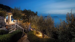 Una propiedad costera con una escalera de piedra que lleva a una zona de piscina, rodeada de olivos y vistas al mar.