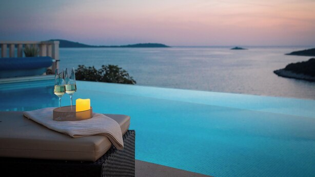 Un área de descanso junto a la piscina con vista al mar, una vela y dos copas de vino.