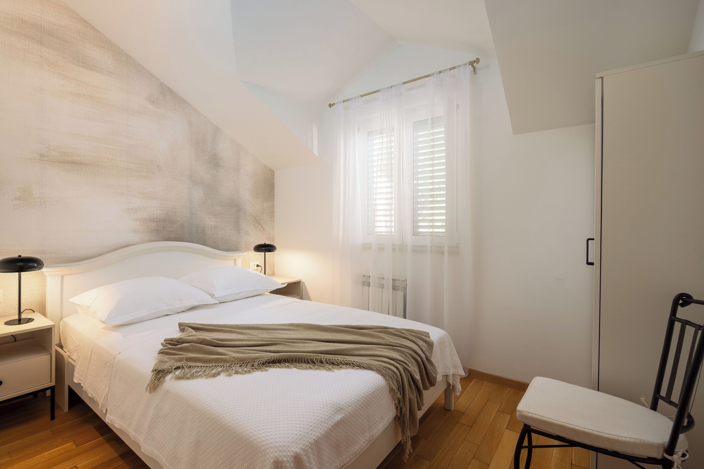 A bedroom with a bed, bedside tables, a chair, and a wardrobe.