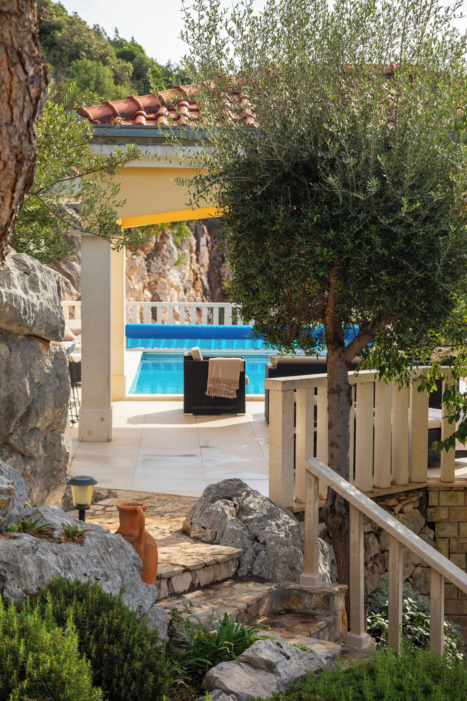 Zona de piscina con un banco de piedra, una valla de madera y vistas a un paisaje montañoso.
