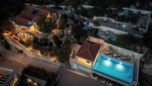 Una casa grande con piscina, terraza techada y un muro de piedra.