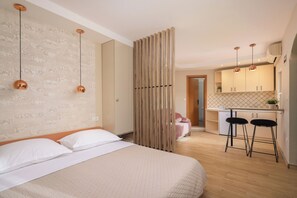 A bedroom with a bed, a wooden partition, and a kitchenette with a countertop and two bar stools.