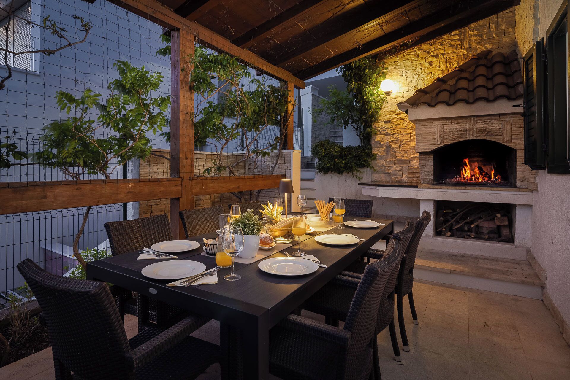 An outdoor dining area with a stone fireplace, wicker chairs, and a table set for four.