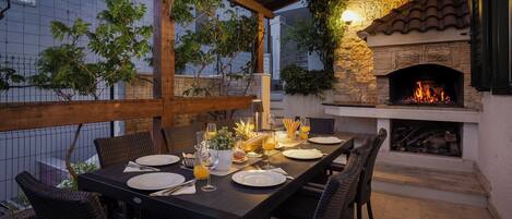 An outdoor dining area with a stone fireplace, wicker chairs, and a table set for four.