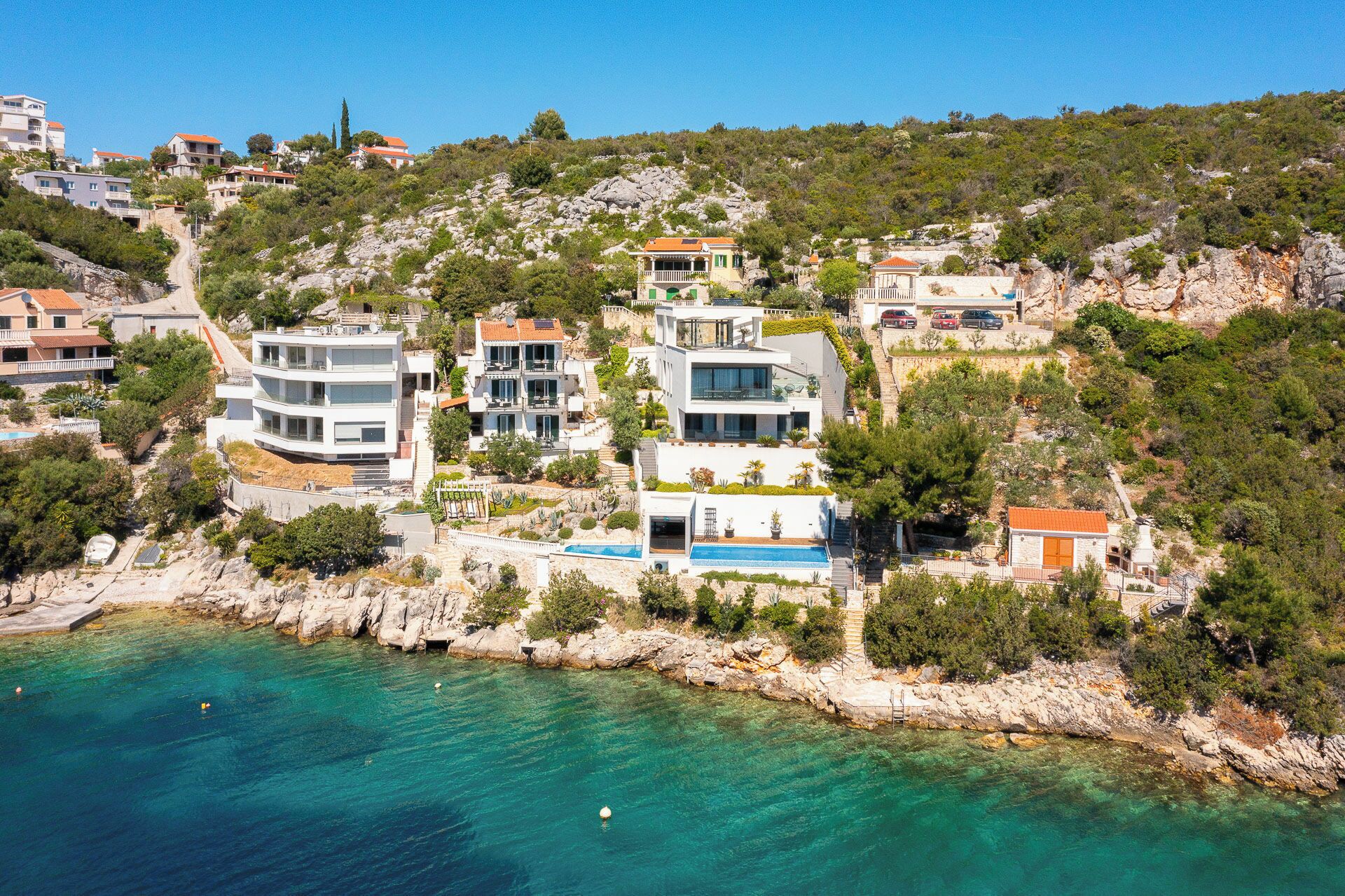 A coastal residential area with modern houses, a clear blue sea, and rocky terrain.