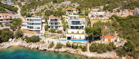 A coastal residential area with modern houses, a clear blue sea, and rocky terrain.