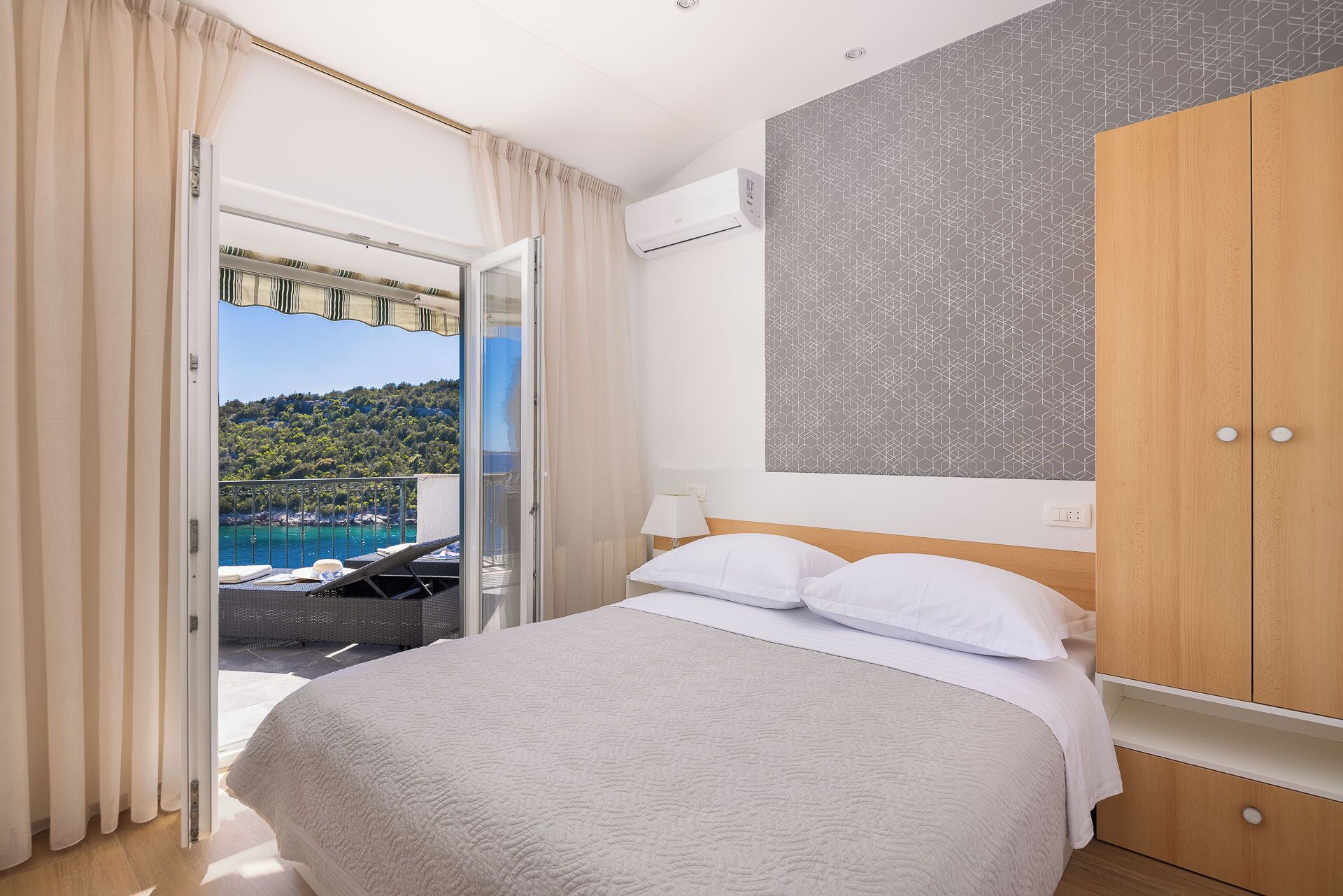 Un dormitorio con cama, armario y vistas a un balcón con piscina y colinas.