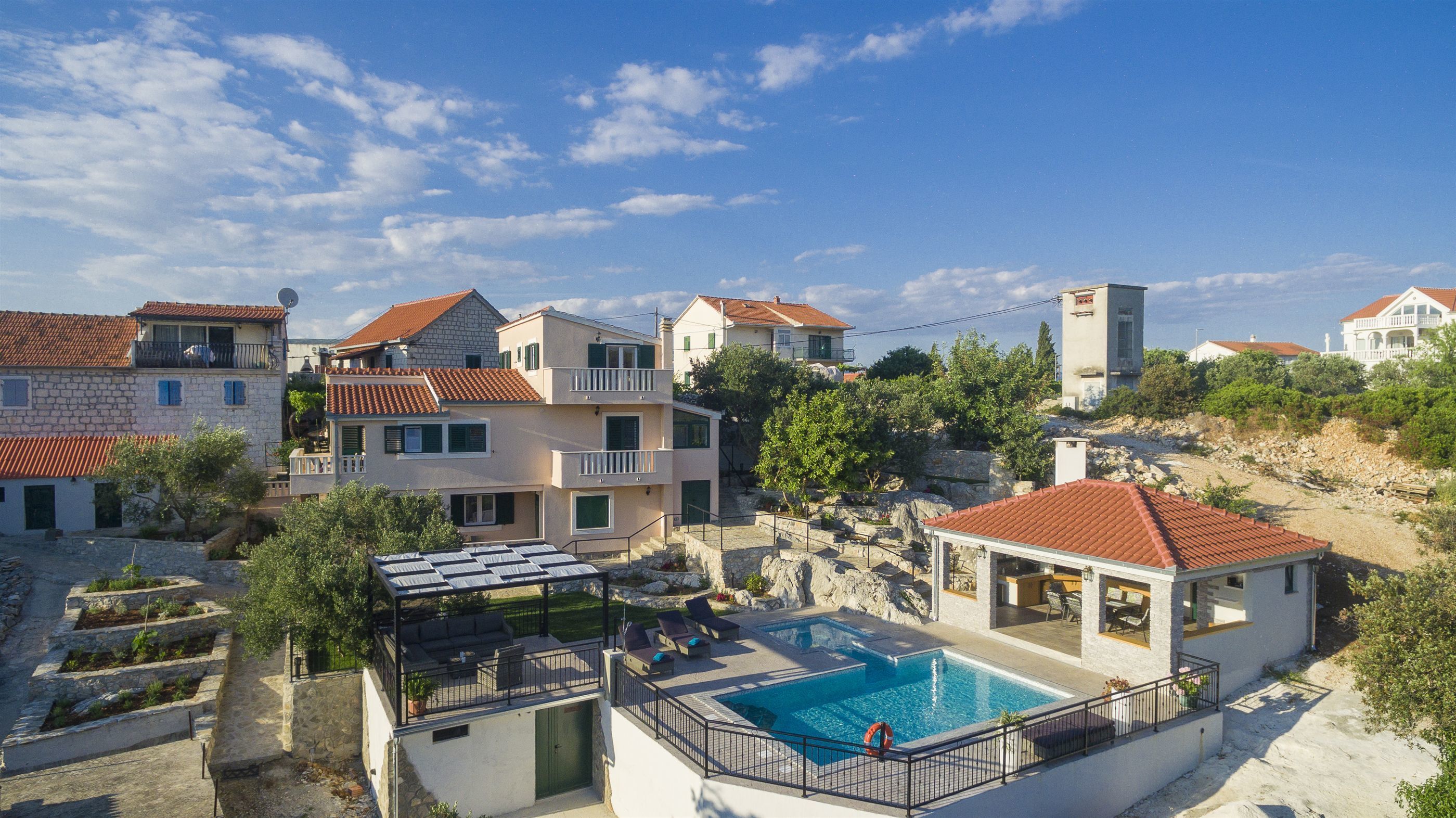 A residential area with a swimming pool, stone buildings, and a clear blue sky.