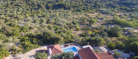 A residential area with a swimming pool, terraced houses, and a hillside with dense vegetation.