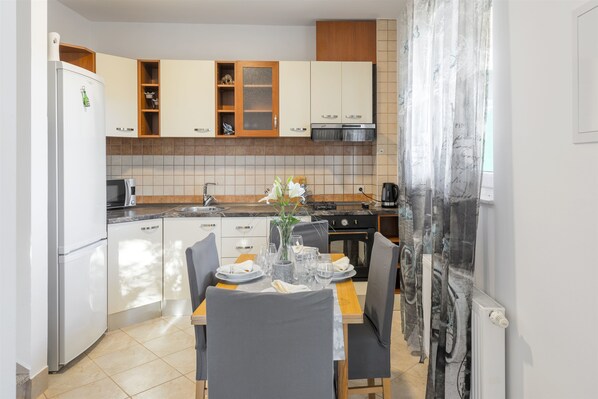 A modern kitchen with white cabinets, a dining table set for four, and a large window with curtains. - Villa Boulder (Okrug Donji)