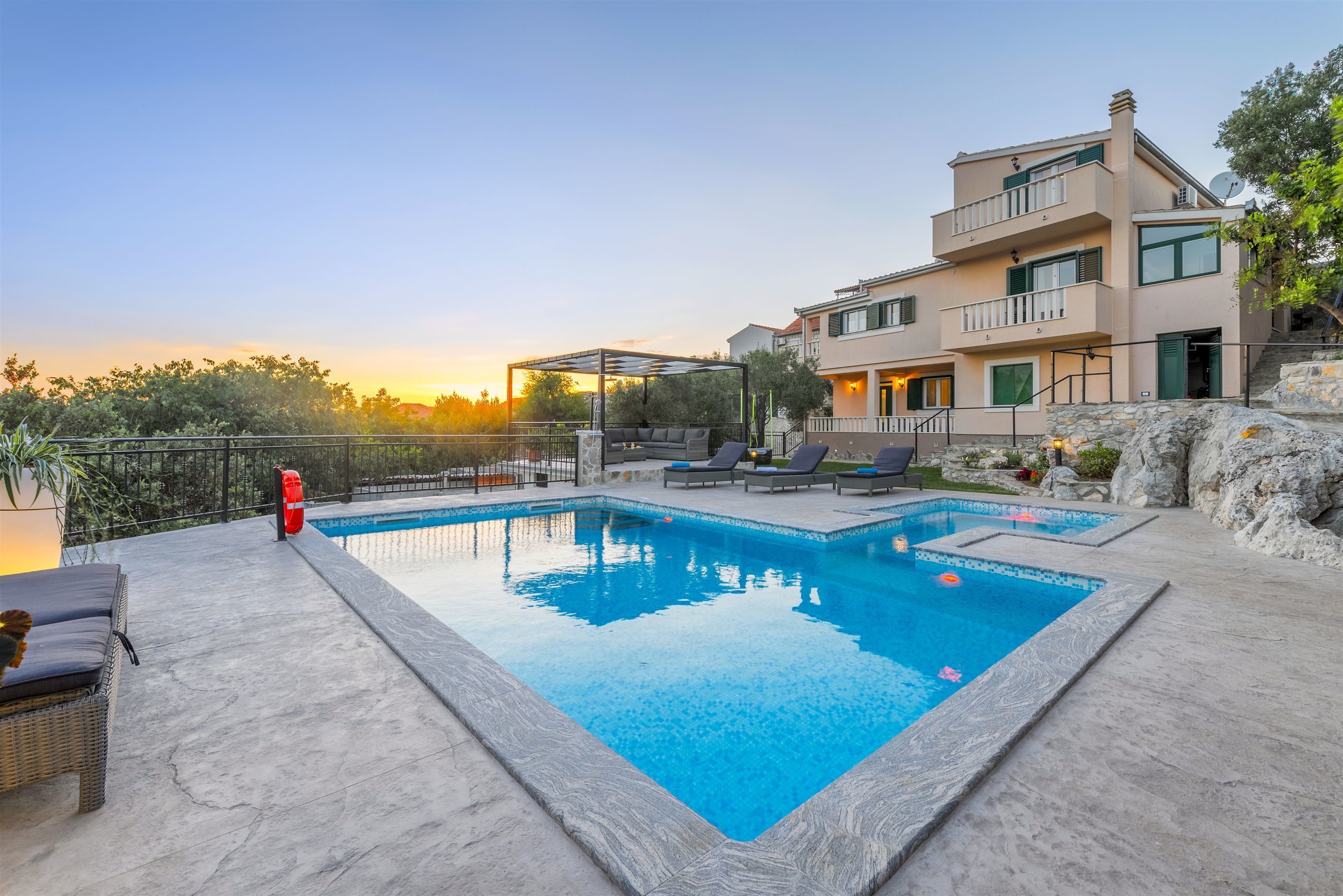 Ein moderner Poolbereich mit Liegestühlen und einer Stein-Terrasse, umgeben von einem mehrstöckigen Gebäude mit Balkonen.