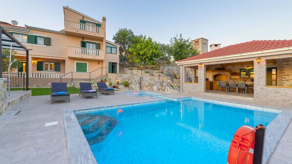 A swimming pool with lounge chairs, a stone wall, and a stone building with a tiled roof. - Villa Boulder (Okrug Donji)