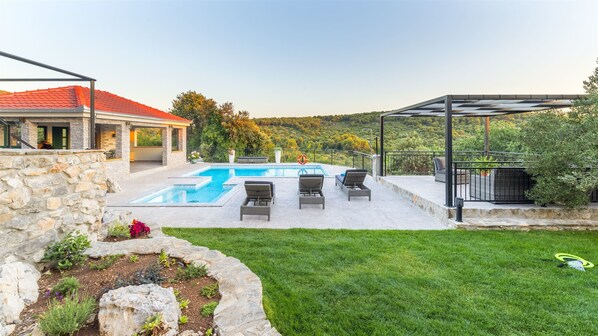 A swimming pool with lounge chairs, a stone wall, and a grassy lawn.