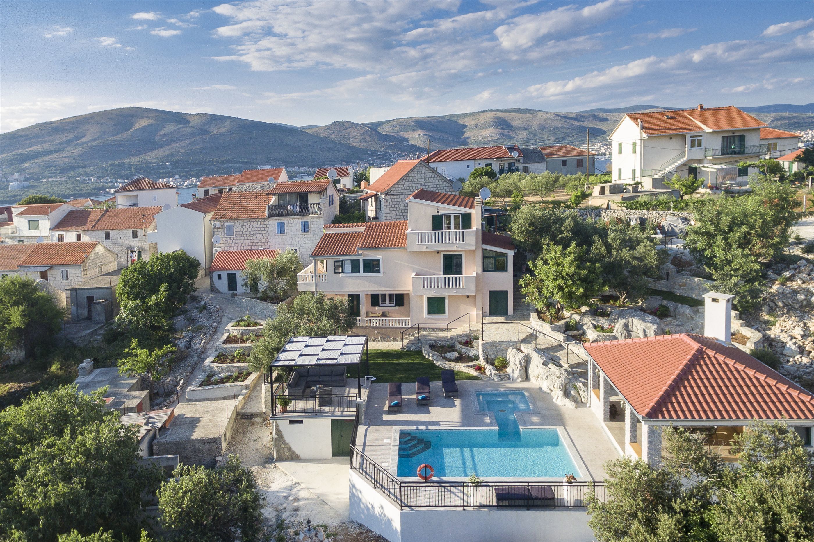 A hillside residential area with houses featuring red-tiled roofs and a central swimming pool.