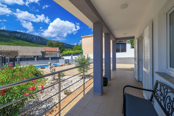 A balcony with a view of a swimming pool, a chair, and a railing.