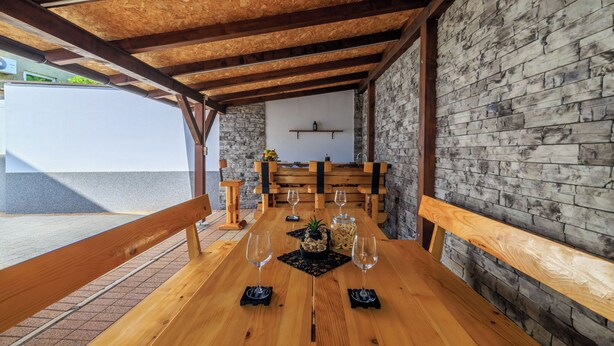 Una mesa de madera con bancos, una planta en maceta y copas de vino preparadas para una comida.