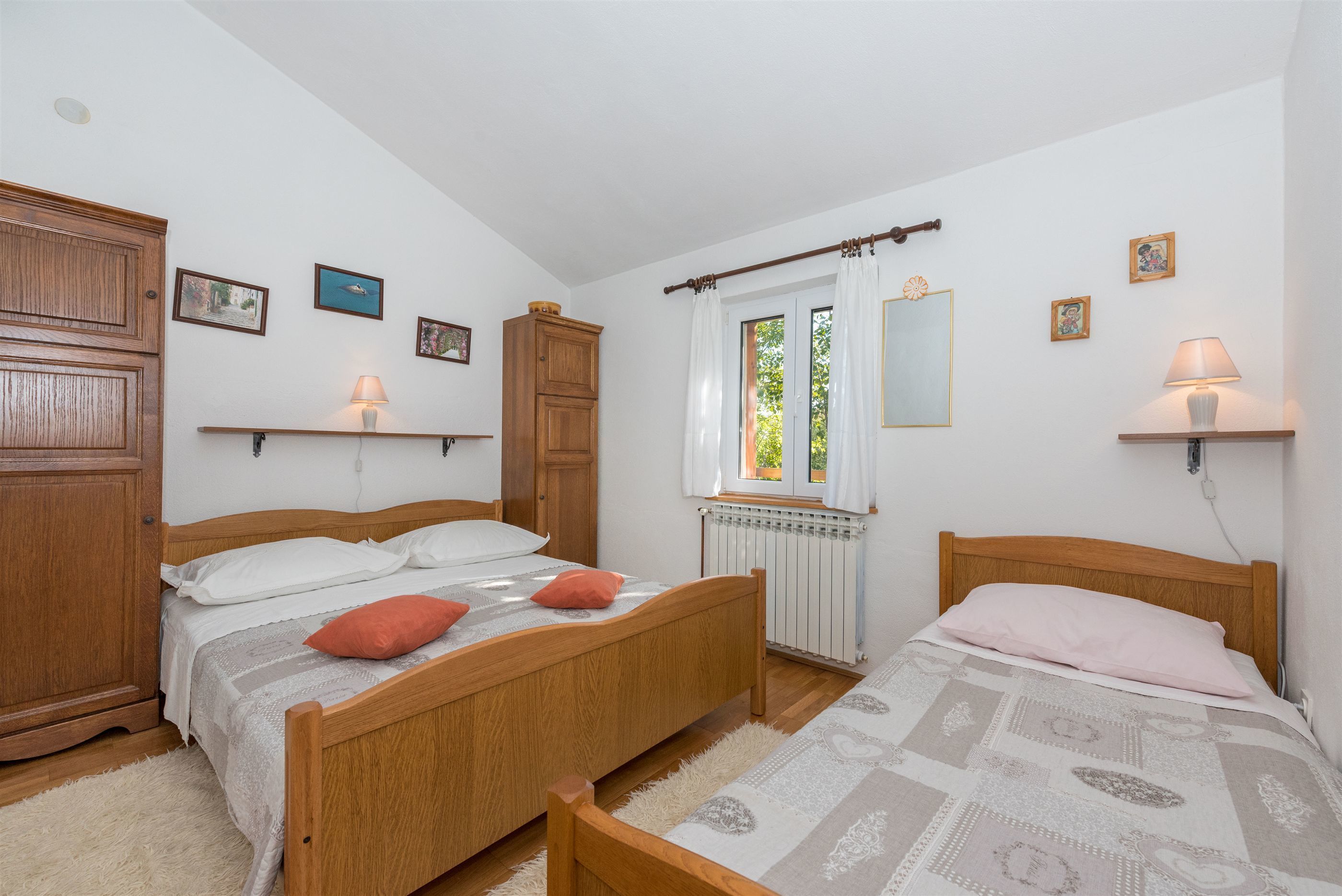 Un dormitorio con dos camas de madera, una ventana con cortinas, un radiador y estantes con lámparas.