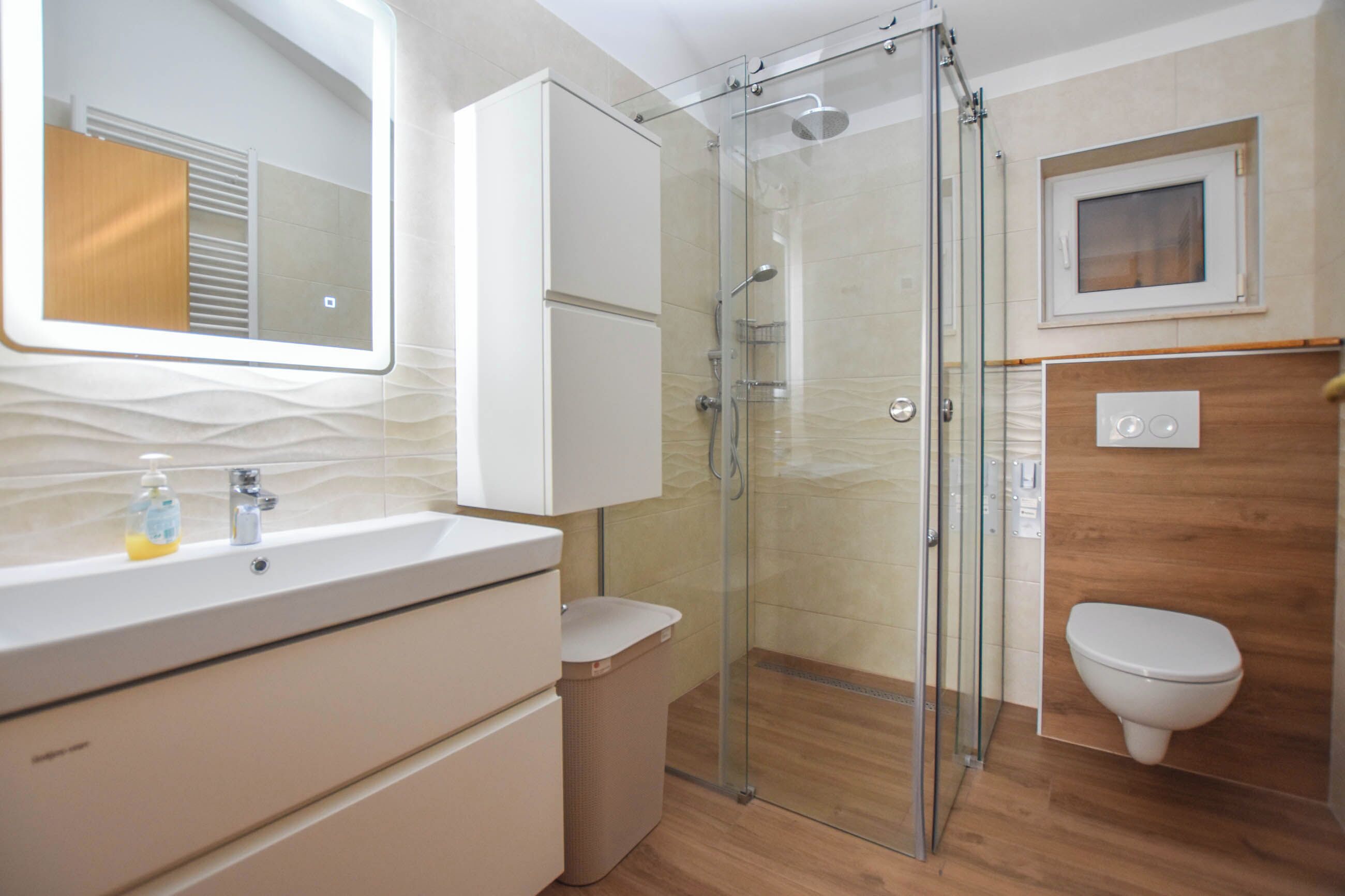 A modern bathroom with a glass shower enclosure, a white sink, and a wooden vanity.