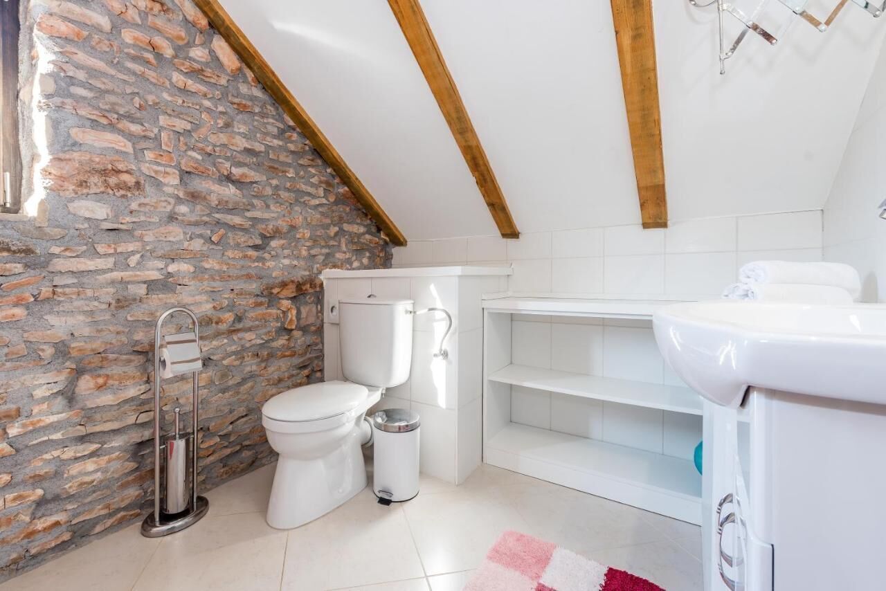 Une salle de bain avec un mur en pierre, des éléments en céramique blanche et une poutre en bois au plafond.