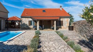 Une maison en pierre avec un toit recouvert de tuiles rouges, une piscine et un chemin en pierre.