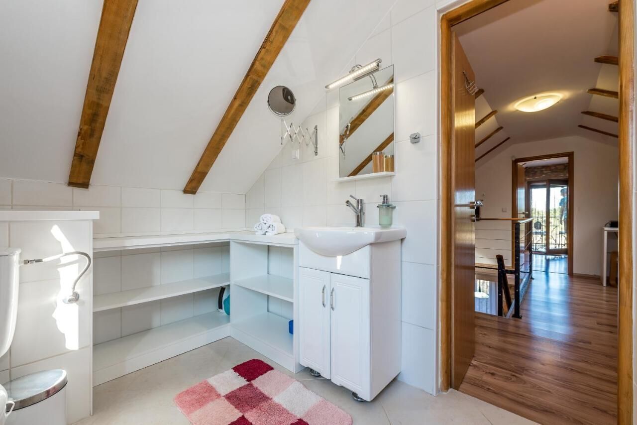 A modern bathroom with a sloped ceiling, a white sink, a mirror, and a shower.