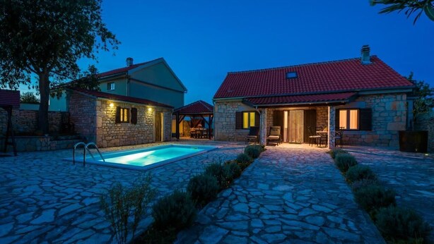 Une maison en pierre dotée d’une piscine, d’un chemin en pierre et d’un espace extérieur aménagé pour se détendre.