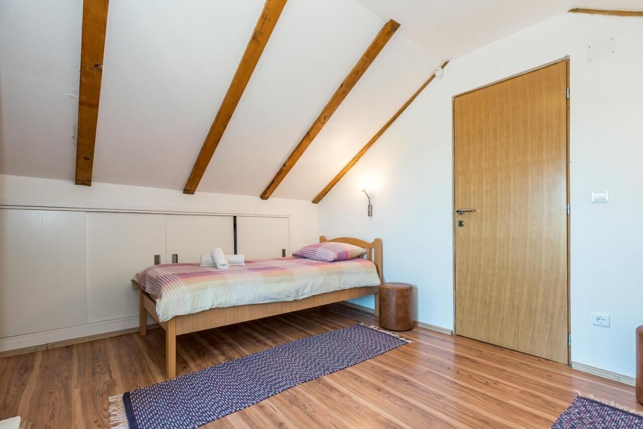 Un dormitorio con una cama de madera, una mesita de noche pequeña, una puerta y un techo inclinado con vigas de madera.