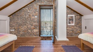 Une chambre avec un mur en pierre, des poutres en bois, un lit et une porte avec un rideau.