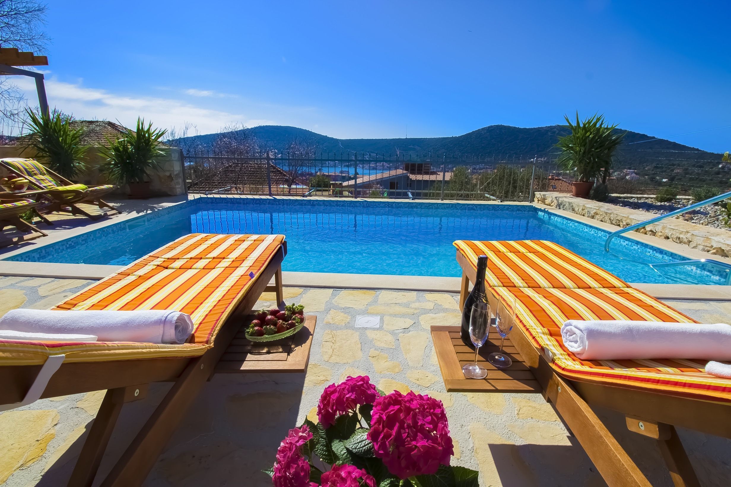 Zona de piscina con dos tumbonas, una copa de vino y un cuenco de fruta.