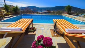 Zona de piscina con dos tumbonas, una copa de vino y un cuenco de fruta.
