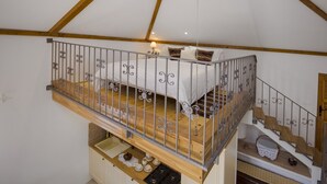 Un dormitorio tipo loft con piso de madera, baranda de metal, una cama y una pequeña mesa con tazas y una tetera.