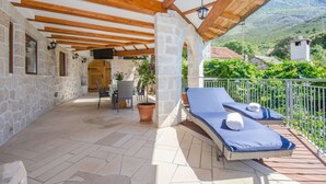 A covered outdoor area with stone walls, wooden beams, a seating area, and a view of the surrounding landscape. - Villa Strnj (Zivogosce)