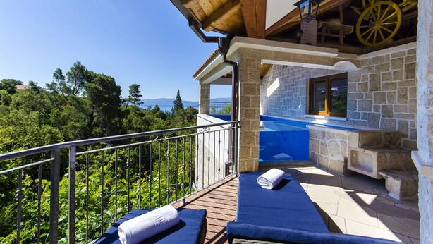 A balcony with a stone wall, a wooden ceiling, and a view of trees and mountains. - Villa Strnj (Zivogosce)