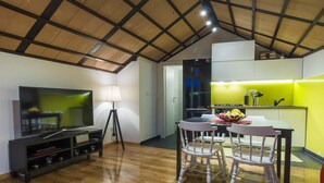 A modern living room with a flat-screen TV, wooden flooring, a dining area with two chairs, and a kitchen with a yellow wall and a refrigerator. - Villa Burica (Vinisce)