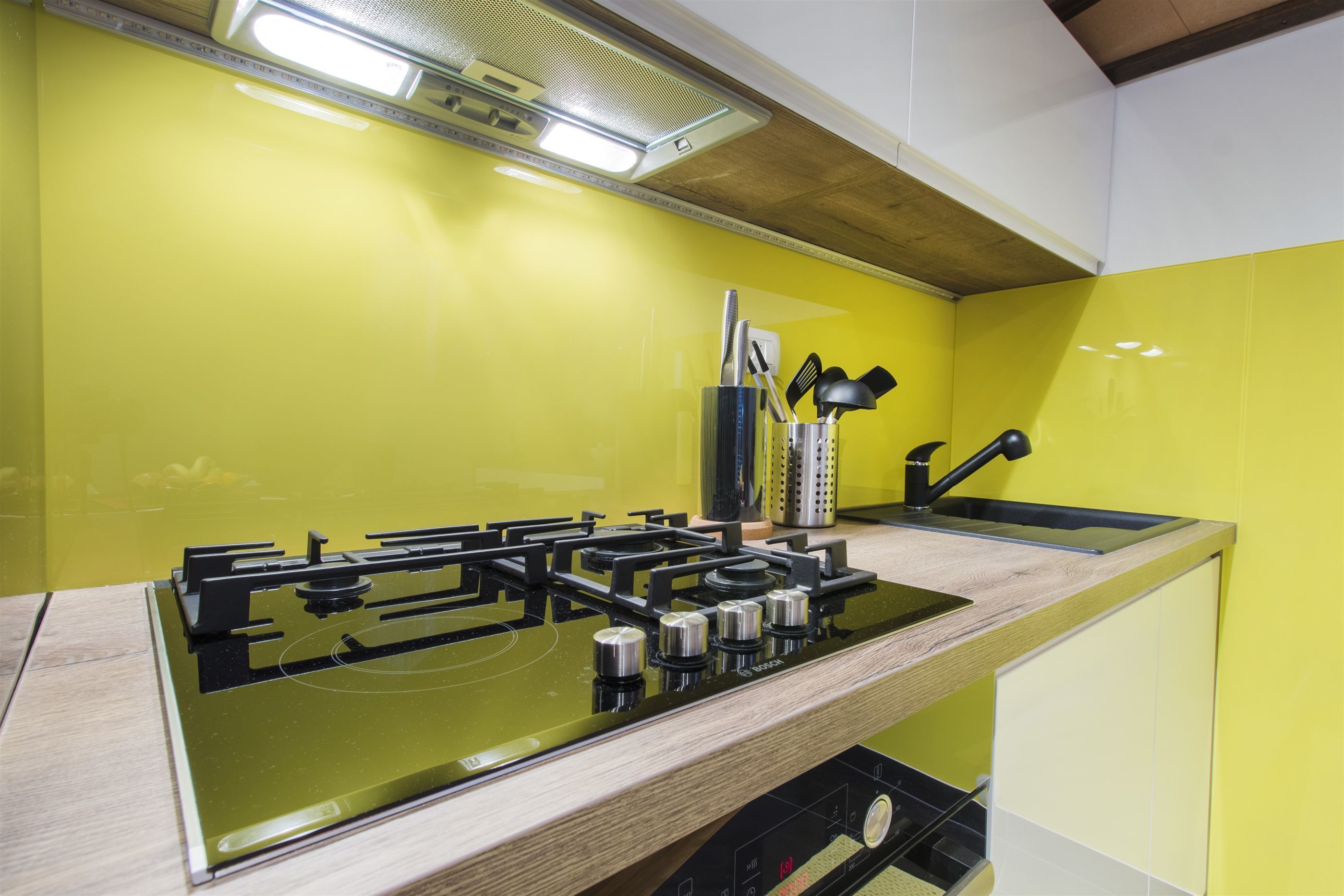 A kitchen with a black stove, a sink, and a yellow backsplash.