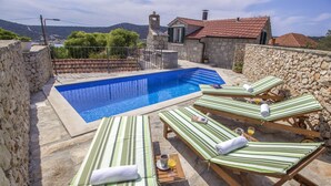 A pool area with lounge chairs and a stone wall. - Villa Burica (Vinisce)