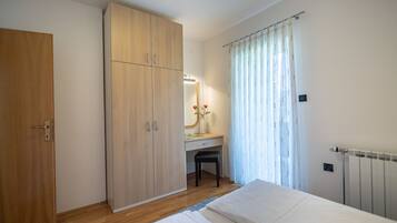 A bedroom with a wooden wardrobe, a desk with a chair, a radiator, and a bed.