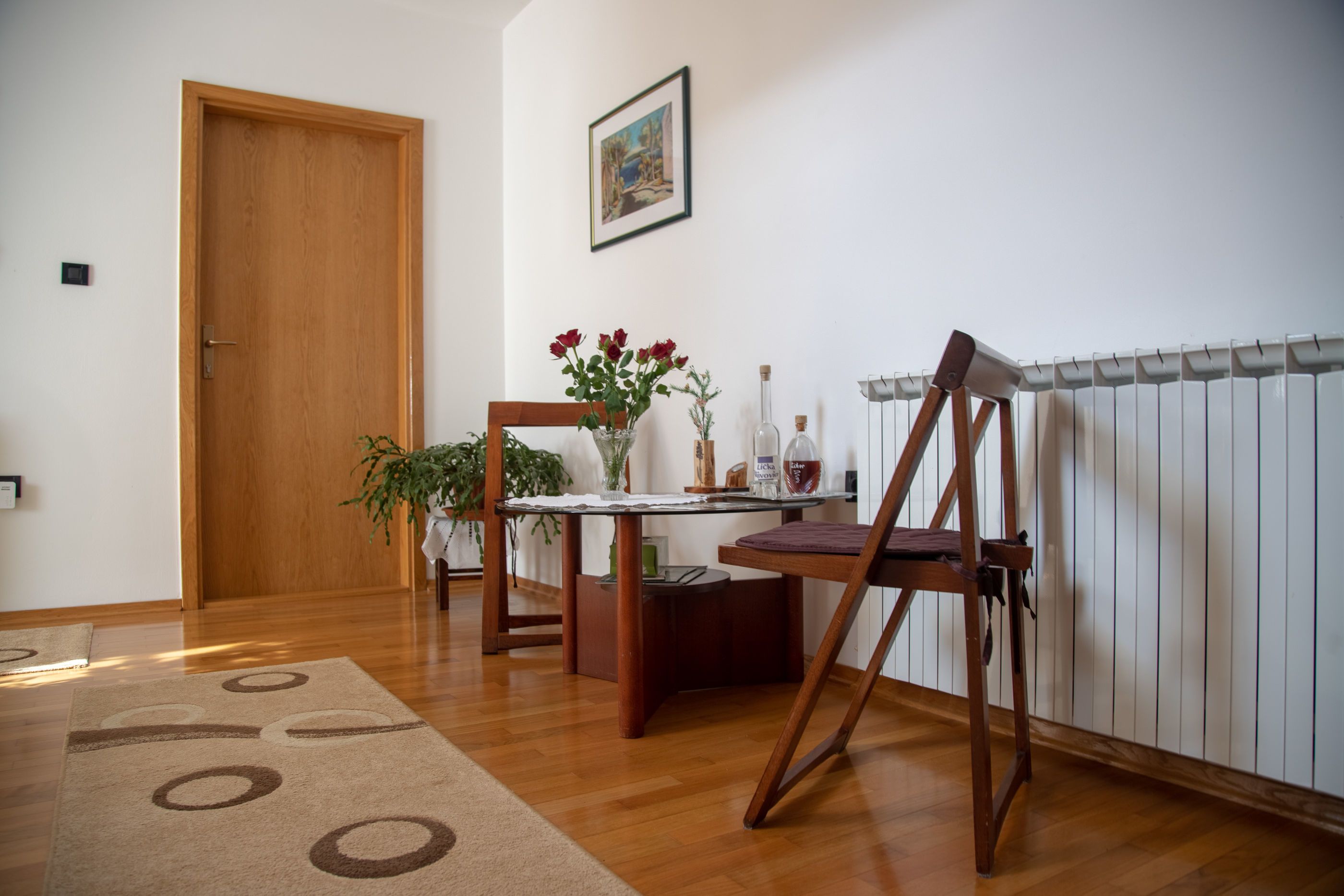 A room with a wooden door, a table with a vase of flowers, a chair, and a radiator.
