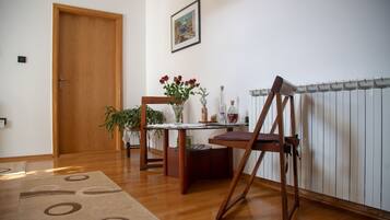 A room with a wooden door, a table with a vase of flowers, a chair, and a radiator.