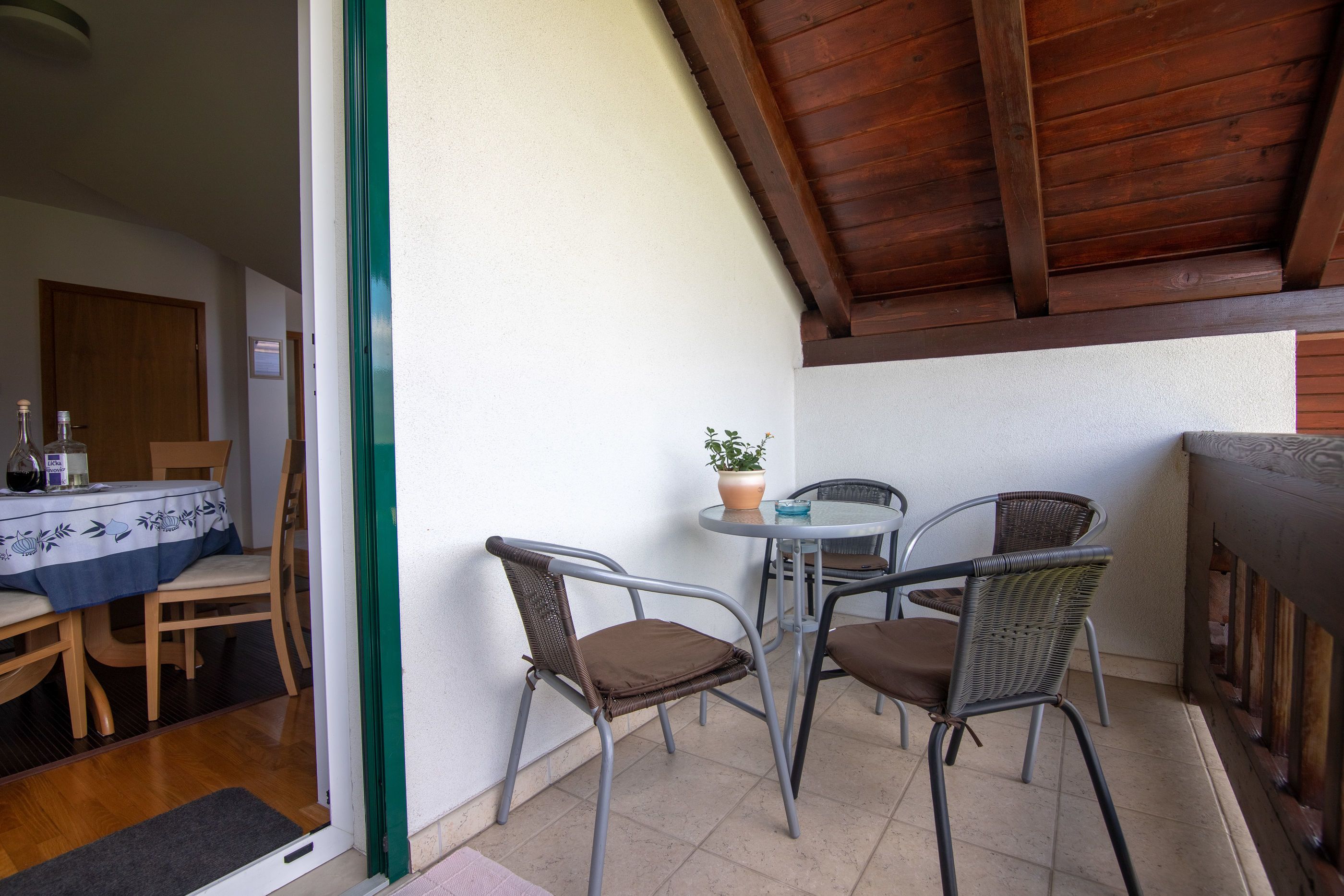 Uma pequena área de pátio com mesa, cadeiras, planta em vaso e teto de madeira.