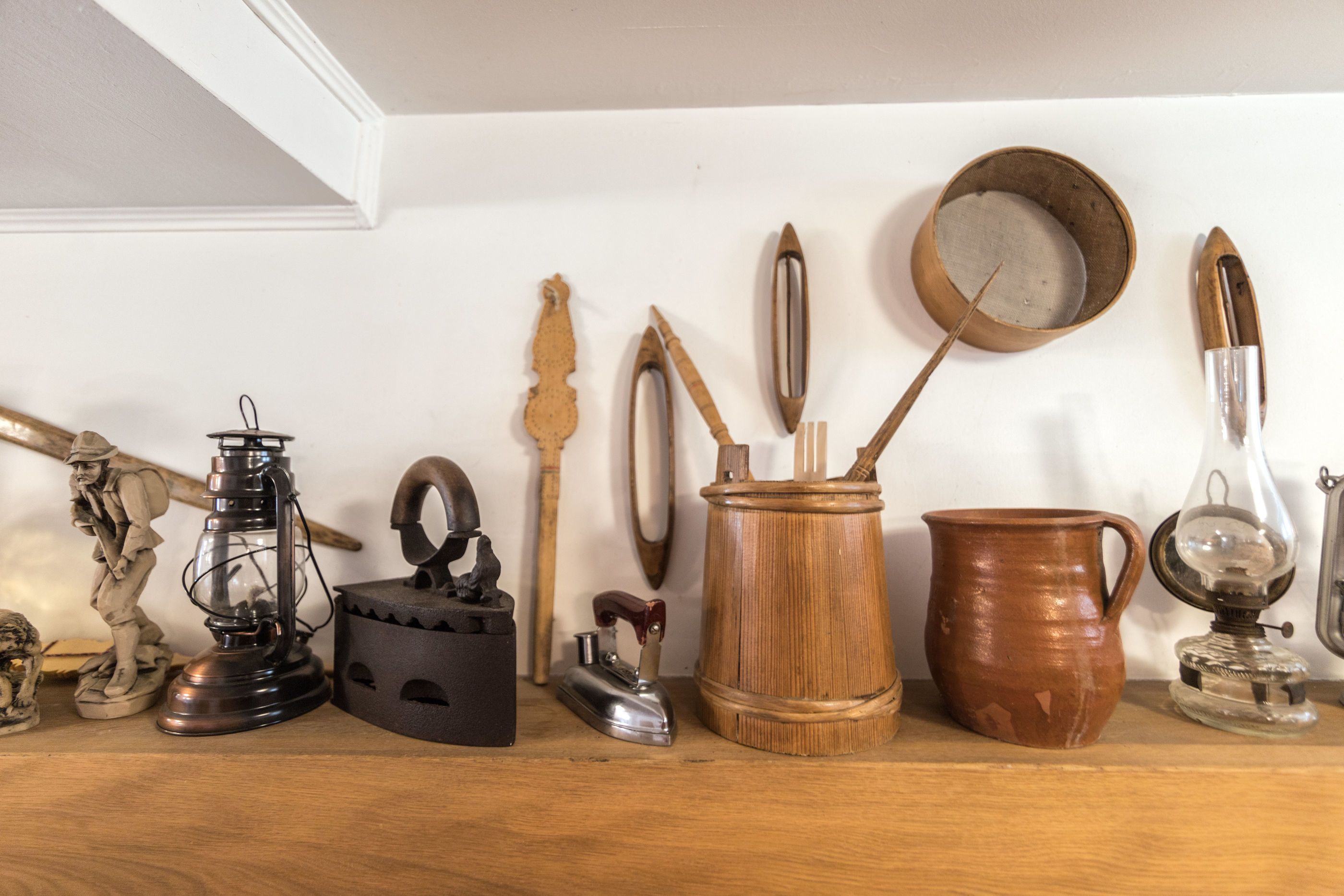 Una repisa con varios objetos antiguos de cocina, como un hervidor de metal, una jarra de madera y una tetera de latón.